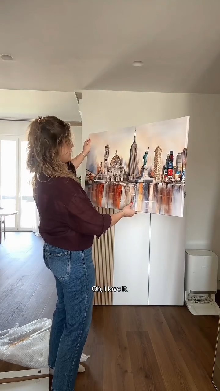 Customer adjusting her custom Florence and New York City skyline canvas on a cabinet in her living room
